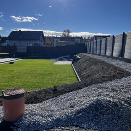 Pavel Auseyeu - Nowo założony ogród z równym trawnikiem, świeżo nasypaną ziemią i wysypanym białym grysem, widoczny włóknina pod kamieniami, w tle domy i wysoka drewniana palisada