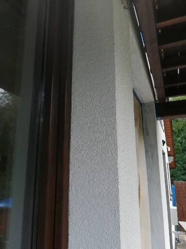 Fragment elewacji budynku z oknem i widoczną fakturą tynku baranka, świeżo pomalowana na szaro kolumna pomiędzy oknami.