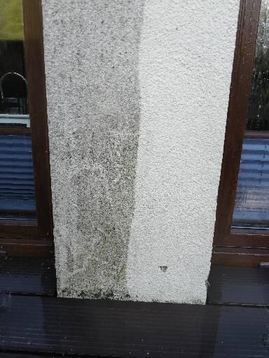 Fragment elewacji budynku z widoczną różnicą przed i po czyszczeniu, z ciemnymi zabrudzeniami po lewej stronie i jasną powierzchnią po prawej, obok okna z brązową ramą.