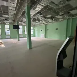 Wnętrze biura po malowaniu ścian na jasnozielony kolor, widoczne kolumny nośne, sufit podwieszany z instalacją wentylacyjną, oraz fragment urządzenia multimedialnego.