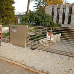 Automatyczna brama posesyjna z poziomych profili, zintegrowana ze skrzynką pocztową, w trakcie montażu, widoczne zabezpieczenia budowlane i samochód dostawczy.