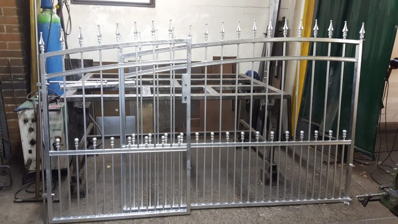 Elementy metalowe ogrodzenia z ozdobnymi zakończeniami w warsztacie, widoczny spawarka i butla z gazem.