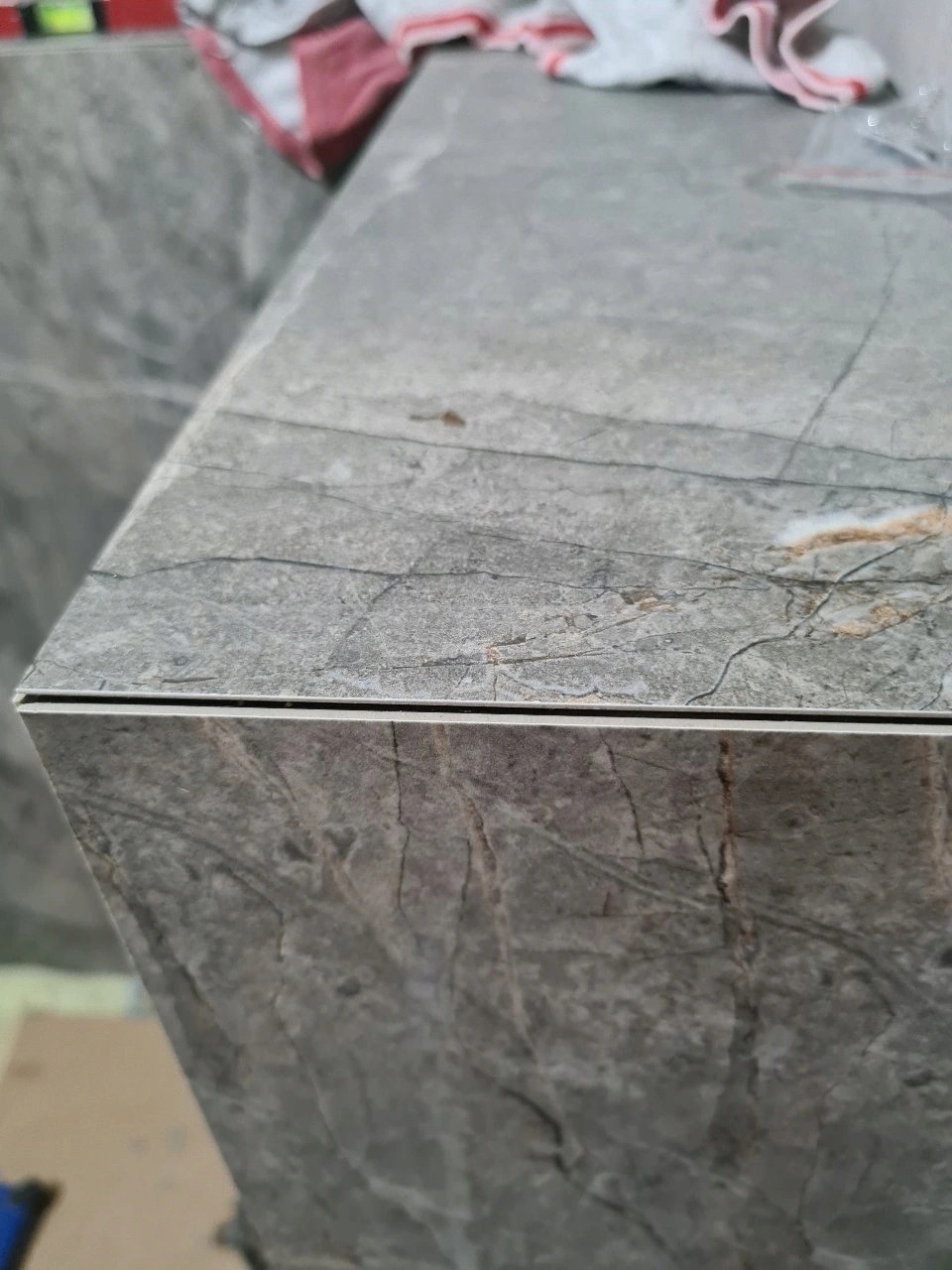 Szczegółowe ujęcie narożnika blatu wykończonego szarą płytką imitującą marmur, z widoczną cienką metalową listwą krawędziową.