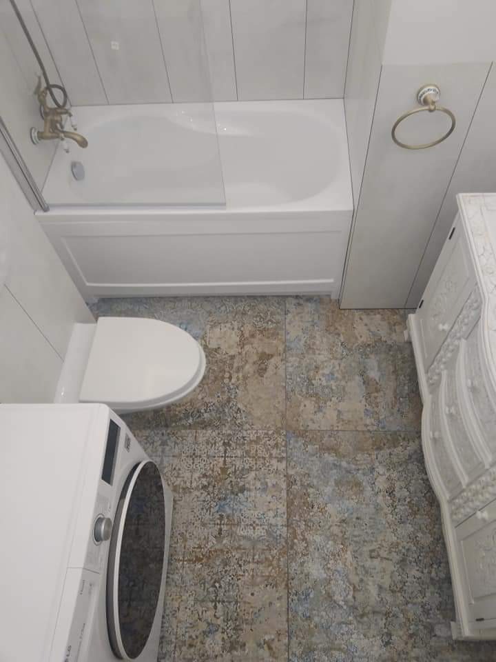 Ustawna łazienka z wanną z parawanem, toaletą, pralką LG i komodą w stylu retro, wykończona płytkami podłogowymi imitującymi przetarty kamień.