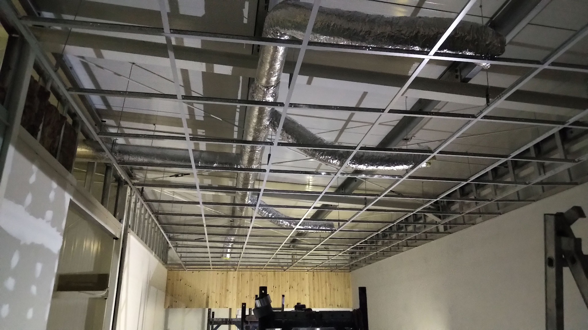 Metalowa konstrukcja podwieszanego sufitu z widocznymi przewodami wentylacyjnymi w przestrzeni między stropem a sufitem, widok z dołu.