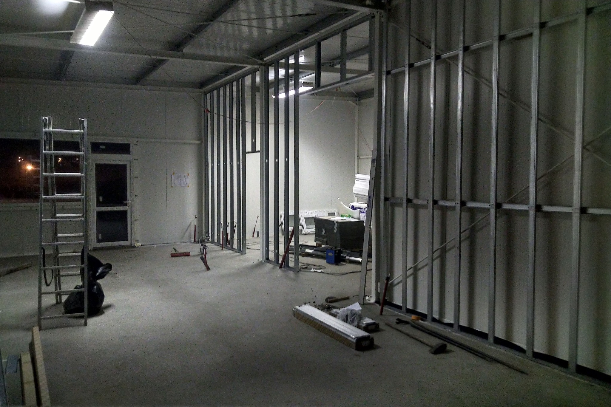 Wnętrze budynku w trakcie budowy dachu z metalową konstrukcją, widoczne narzędzia, drabina i materiały budowlane.