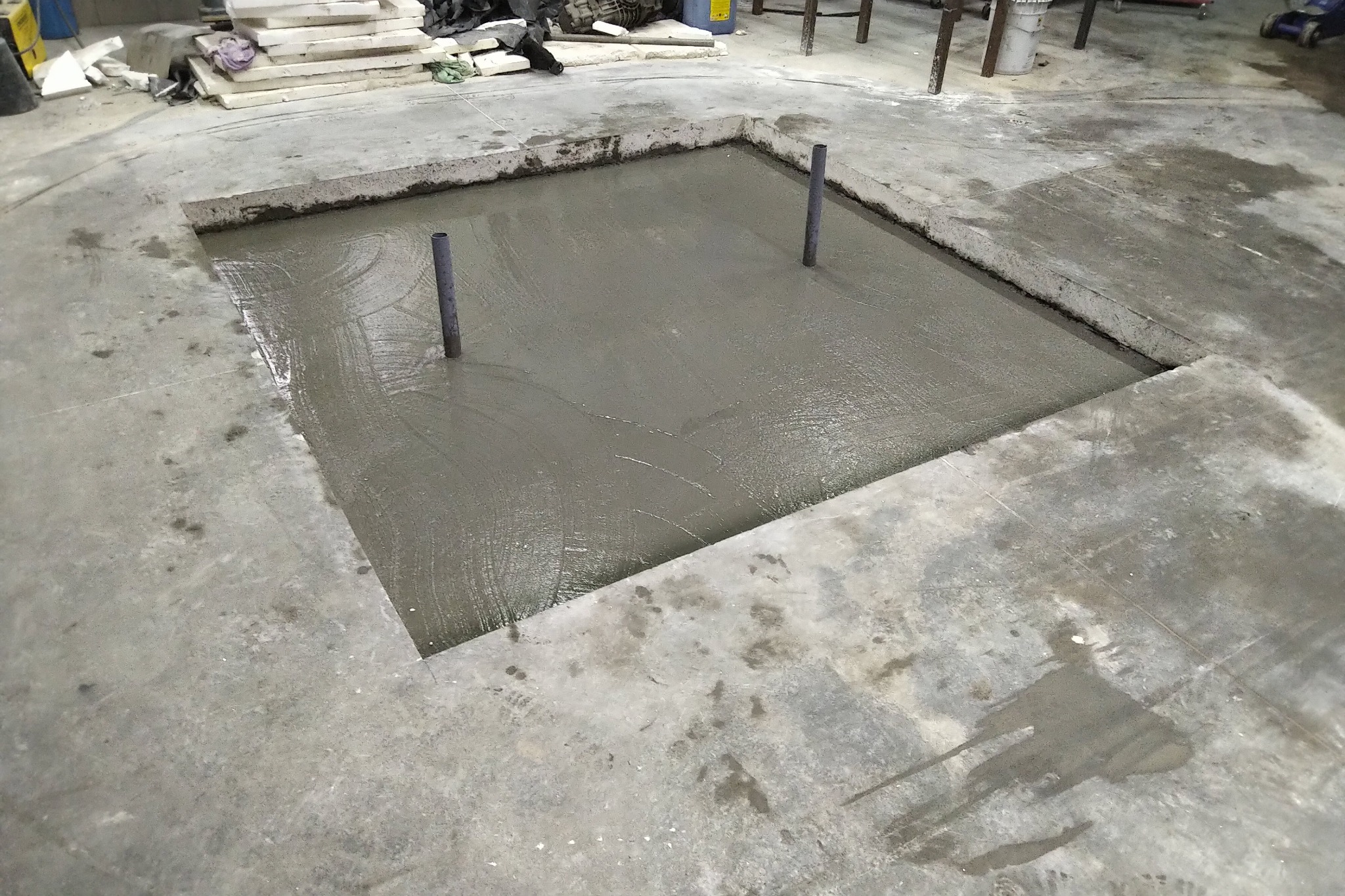Wylewka betonowa z dwoma pionowo wystającymi rurami w wyciętym fragmencie posadzki, widoczne ślady po pracy na betonie.