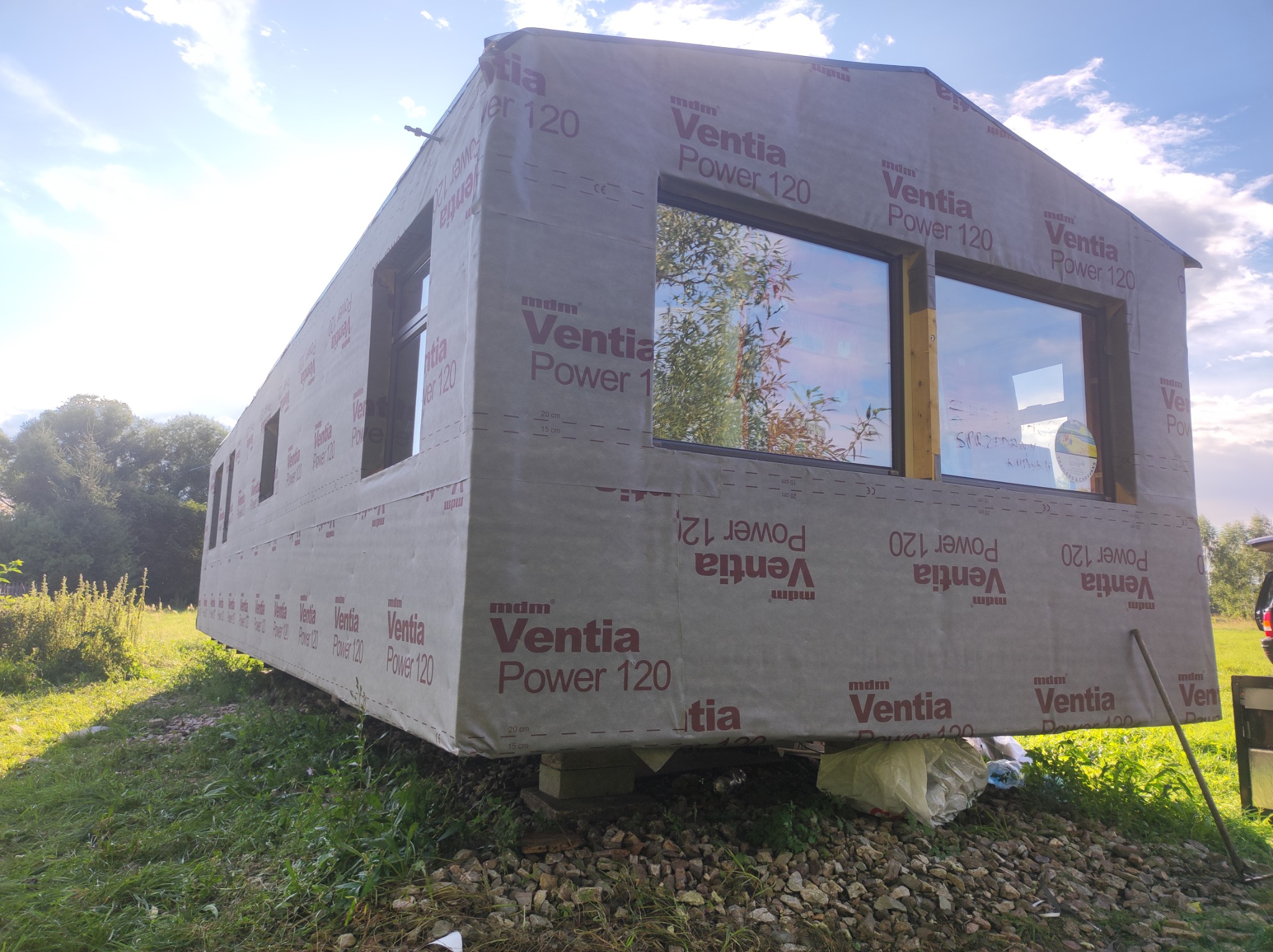 Budynek w trakcie ocieplania, pokryty membraną dachową Ventia Power 120, widoczne okna, tło z zielenią i błękitnym niebem.