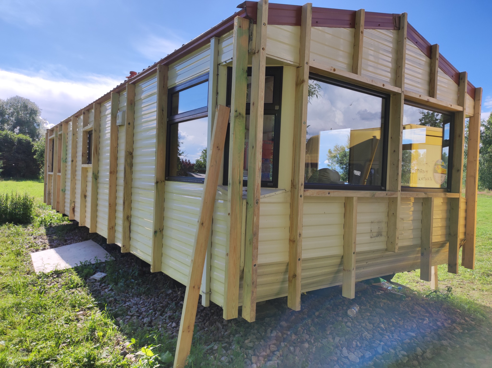 Konstrukcja szkieletowa domu mobilnego z widoczną więźbą dachową w trakcie budowy, jasne panele ścienne, drewniane słupki i krokwie, odbicie w oknach.