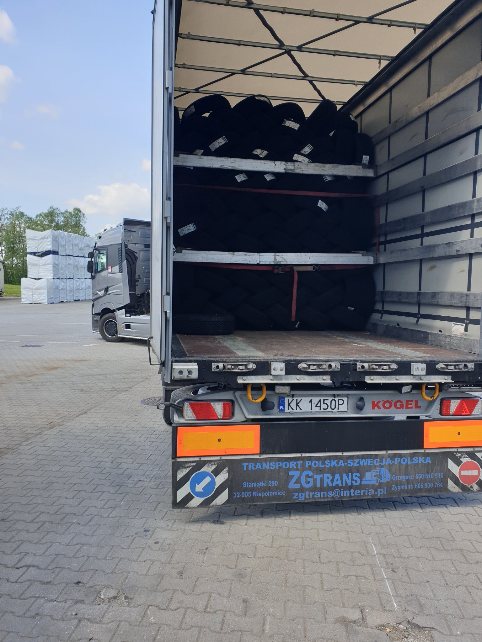 Wnętrze naczepy wypełnione oponami ułożonymi na półkach, widoczny tył naczepy z tablicą rejestracyjną i logo firmy transportowej ZGTRANS realizującej transport Polska-Szwecja-Polska.