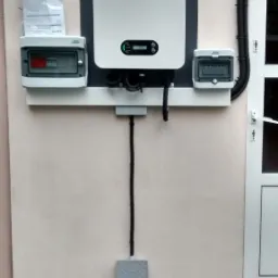 Zamontowany inwerter SOFAR z zabezpieczeniami i licznikiem na ścianie budynku, widoczne okablowanie i skrzynka przyłączeniowa.