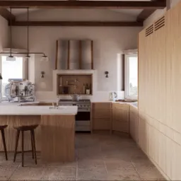 Jasna kuchnia w stylu rustykalnym z drewnianymi belkami, wyspą i regałem. Na blacie ekspres do kawy, a nad kuchenką dekoracyjny okap. Naturalne światło wpada przez okna.