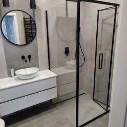 Łukasz - Nowoczesna łazienka z kabiną prysznicową typu walk-in z czarnymi ramami, umywalką nablatową i okrągłym lustrem z czarną ramą, oświetlona wiszącymi lampami tubami.