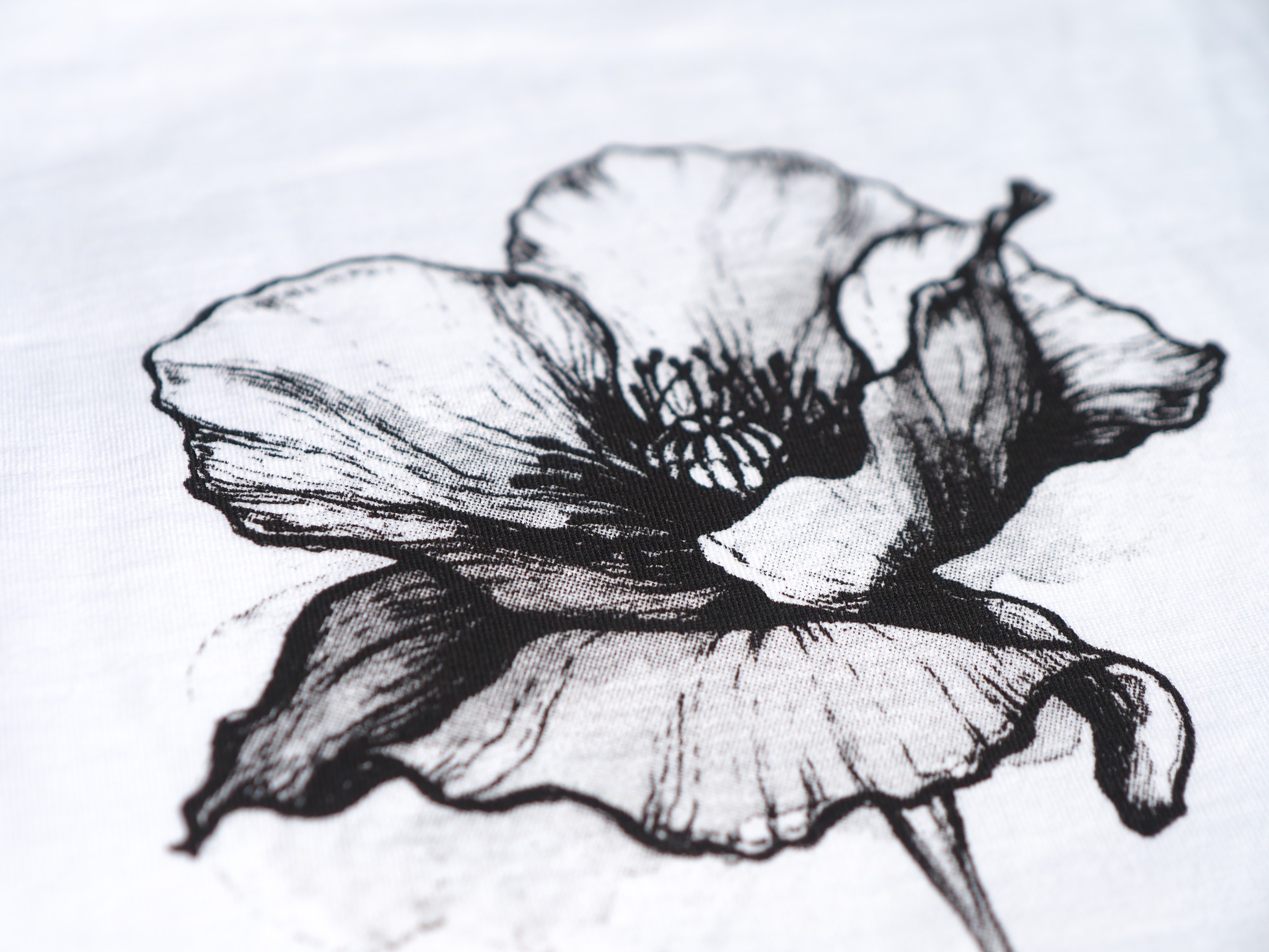 Czarno-biały nadruk maku na białej koszulce, widoczne detale tkaniny i delikatne cieniowanie grafiki.