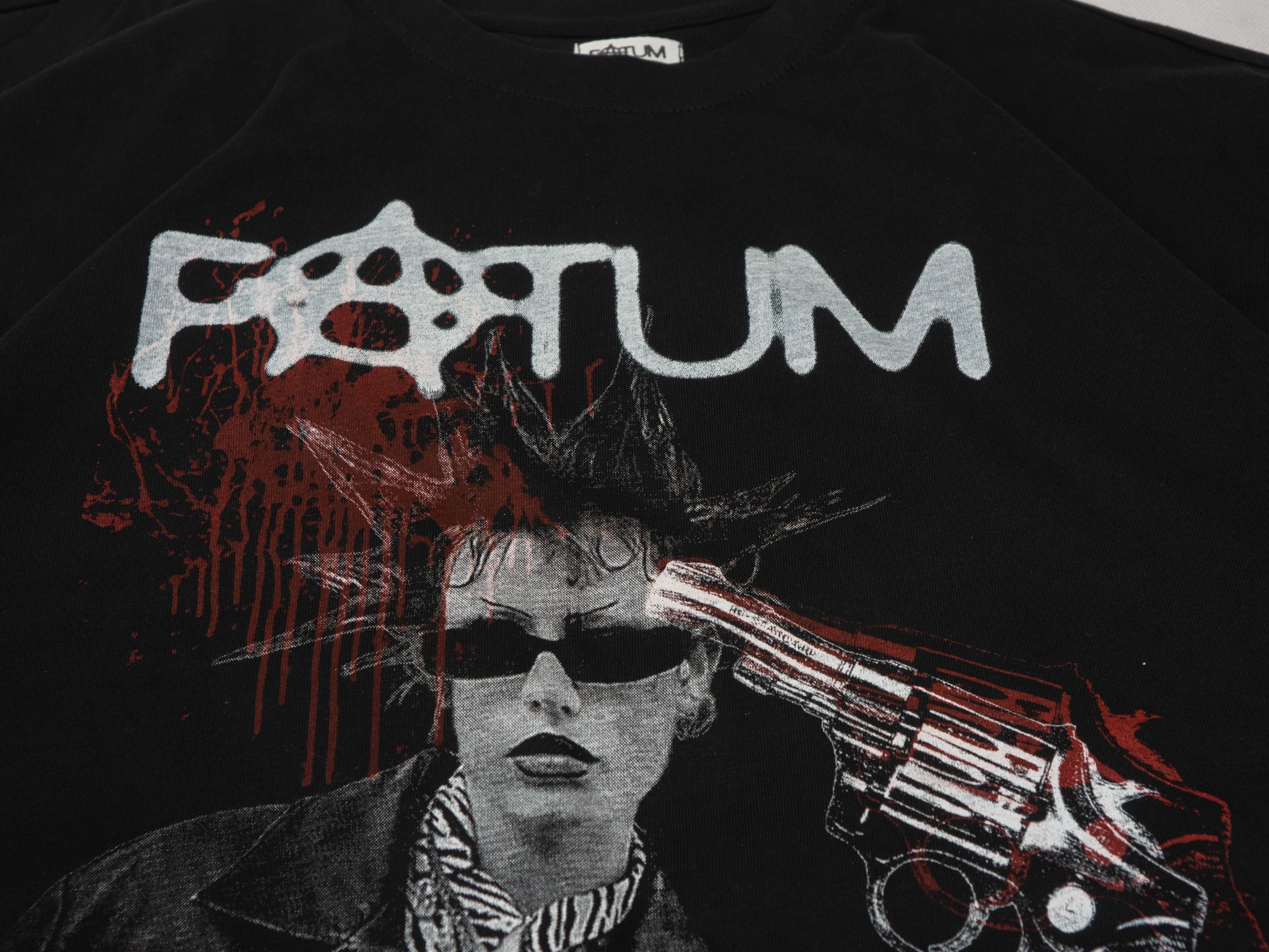 Czarna koszulka z nadrukiem punkowej postaci z pistoletem i efektem rozpryskującej się farby, podkreślona białą czcionką z nazwą 'Fortum'.