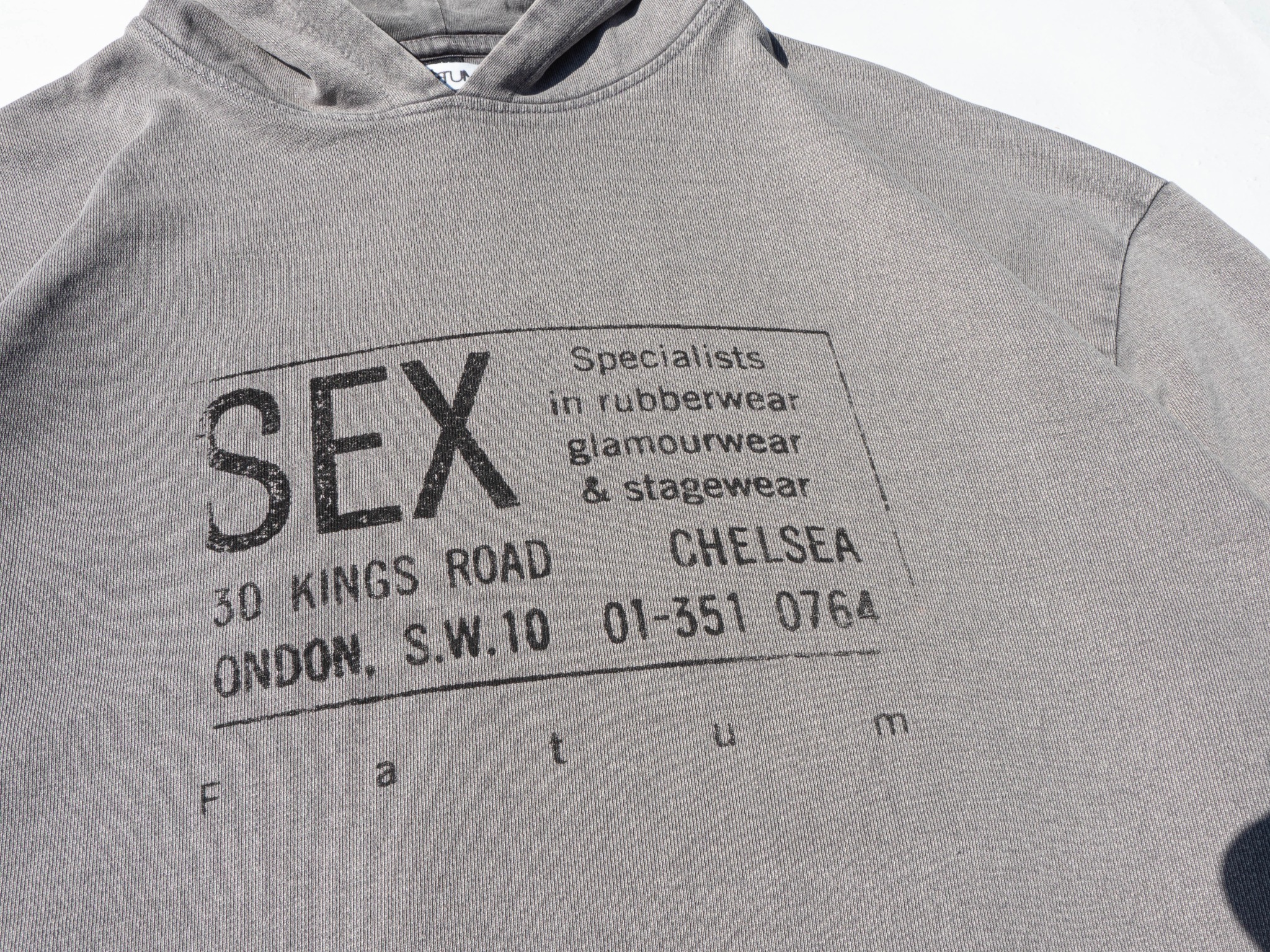 Szara bluza z kapturem z nadrukiem w stylu vintage, zawierającym tekst 'SEX', adres 30 Kings Road, Londyn i informację o specjalizacji w rubberwear, glamourwear i stagewear.