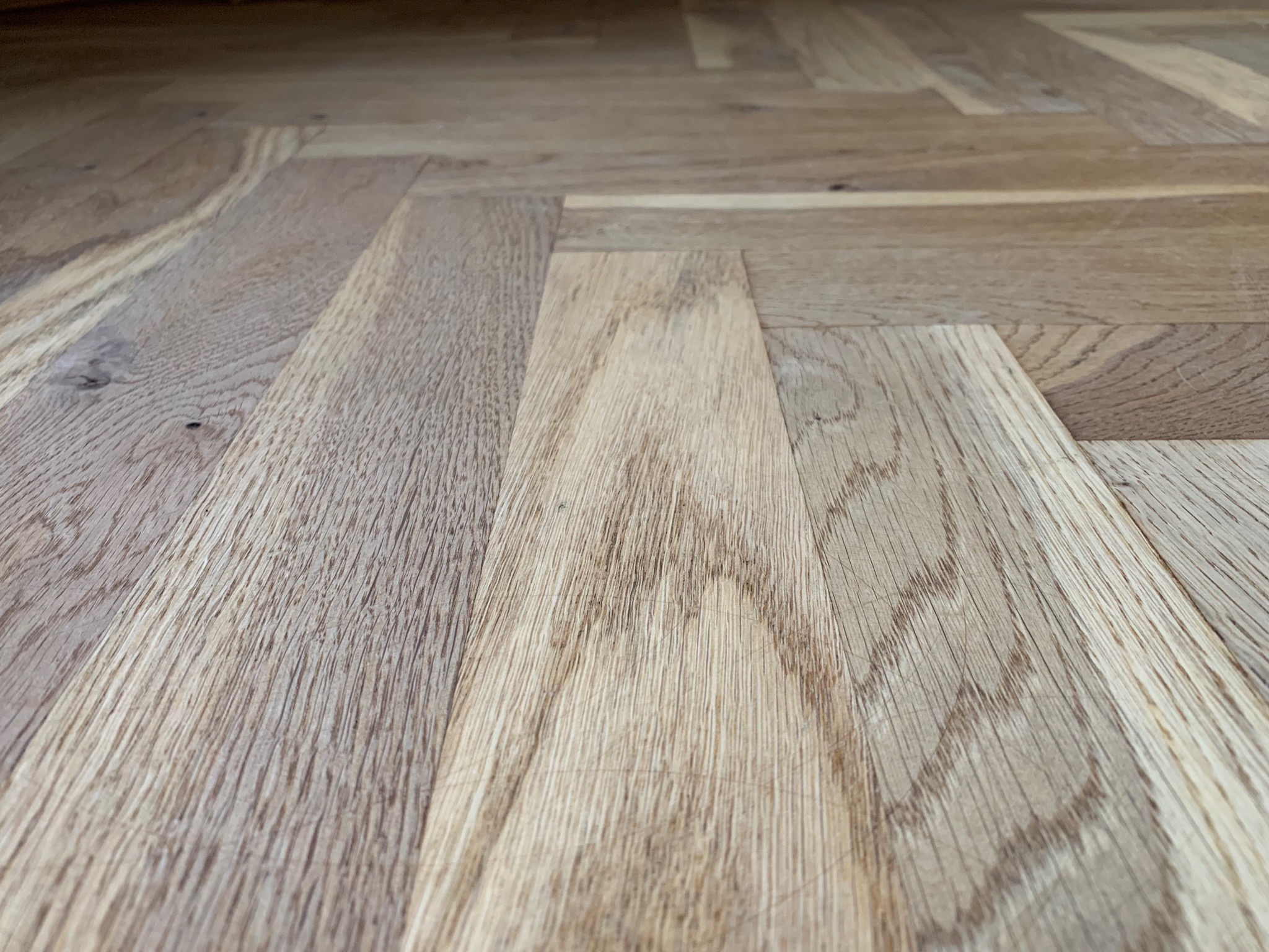 Jasne, drewniane panele ułożone w jodełkę, z widoczną strukturą drewna i subtelnym połyskiem.