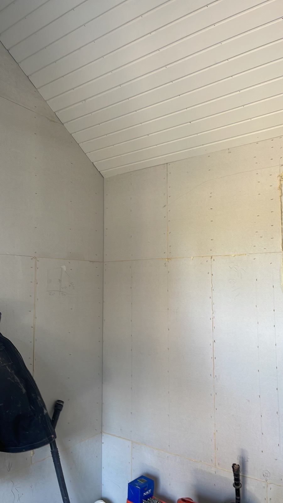 Wnętrze w trakcie prac wykończeniowych: ściany pokryte płytami gipsowo-kartonowymi z widocznymi łączeniami, sufit z paneli PCV, narzędzia i materiały budowlane w tle.