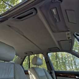 Grabowsky Performance - Wnętrze samochodu z widoczną szarą tapicerką sufitową, skórzanymi siedzeniami i drewnianym wykończeniem deski rozdzielczej; widok z dołu na otwarty szyberdach i drzewa na zewnątrz.