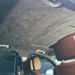 Wnętrze samochodu z nową, szarą podsufitką zamszową oraz brązowymi skórzanymi zagłówkami, widok z dołu.