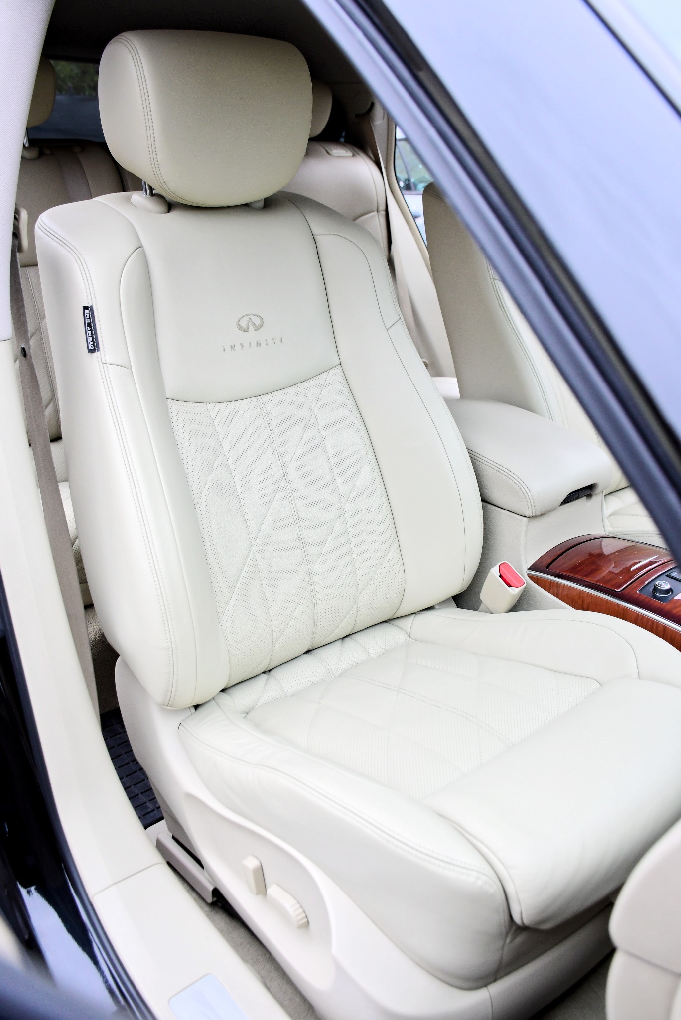 Jasna skórzana tapicerka fotela samochodowego marki Infiniti z pikowaniem w romby i widocznym logo na zagłówku.