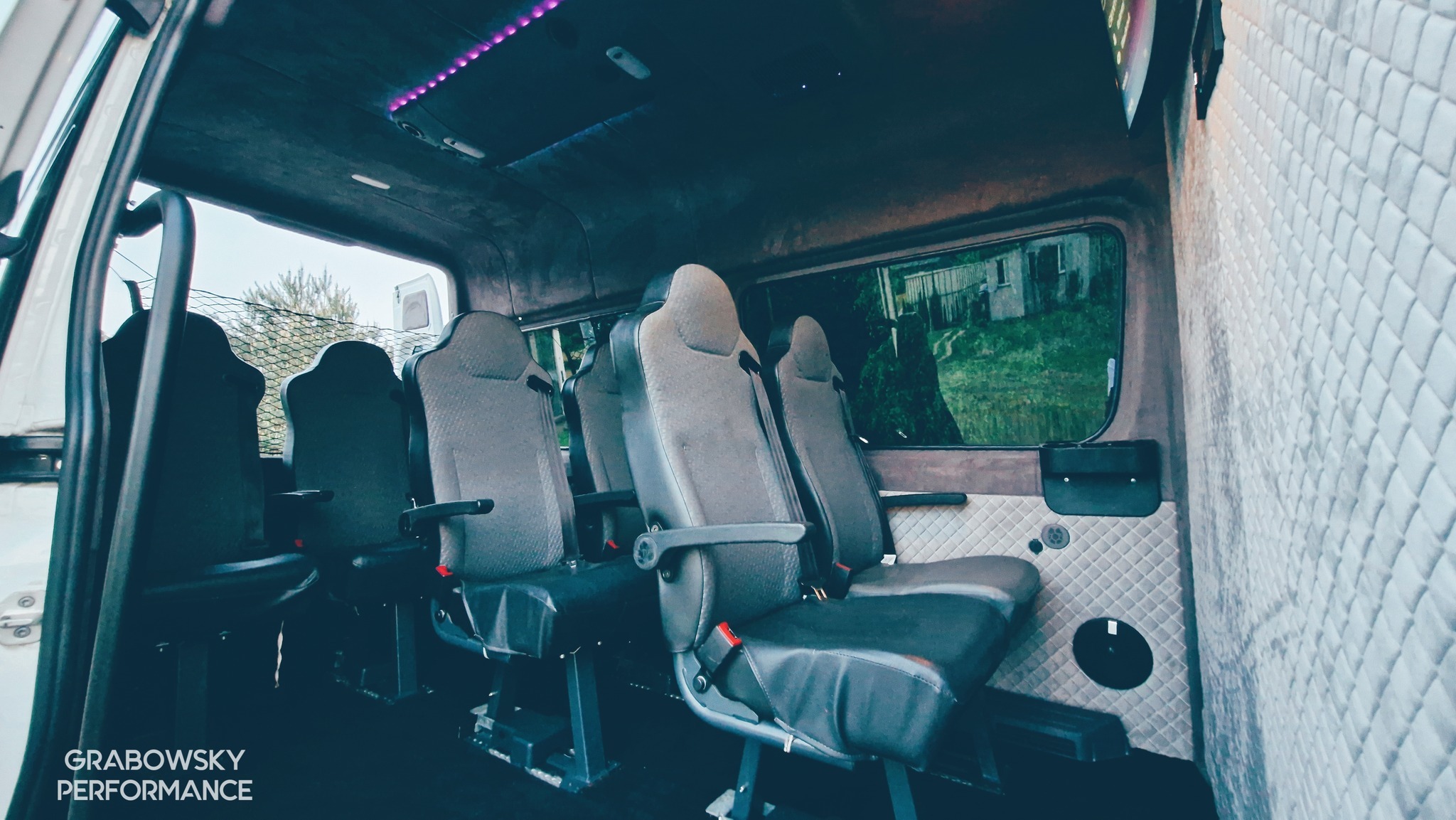 Wnętrze busa po renowacji tapicerskiej: szare fotele z czarnymi elementami, pikowana biała tapicerka ścienna, oświetlenie LED podsufitki.
