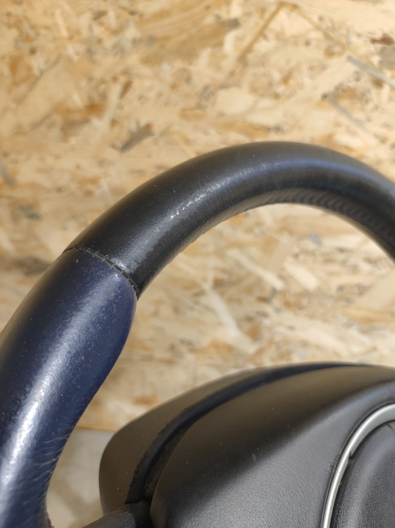 Fragment kierownicy samochodowej z widocznym łączeniem dwóch kolorów skóry: granatowego i czarnego, na tle płyty OSB.