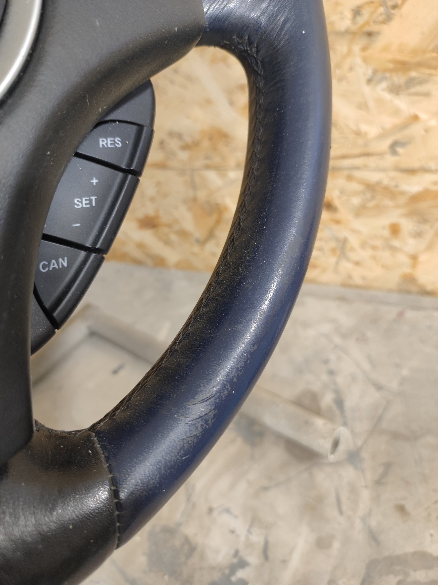 Fragment czarnej kierownicy samochodowej z przyciskami sterowania, widoczne ślady użytkowania i delikatne przetarcia na skórze.