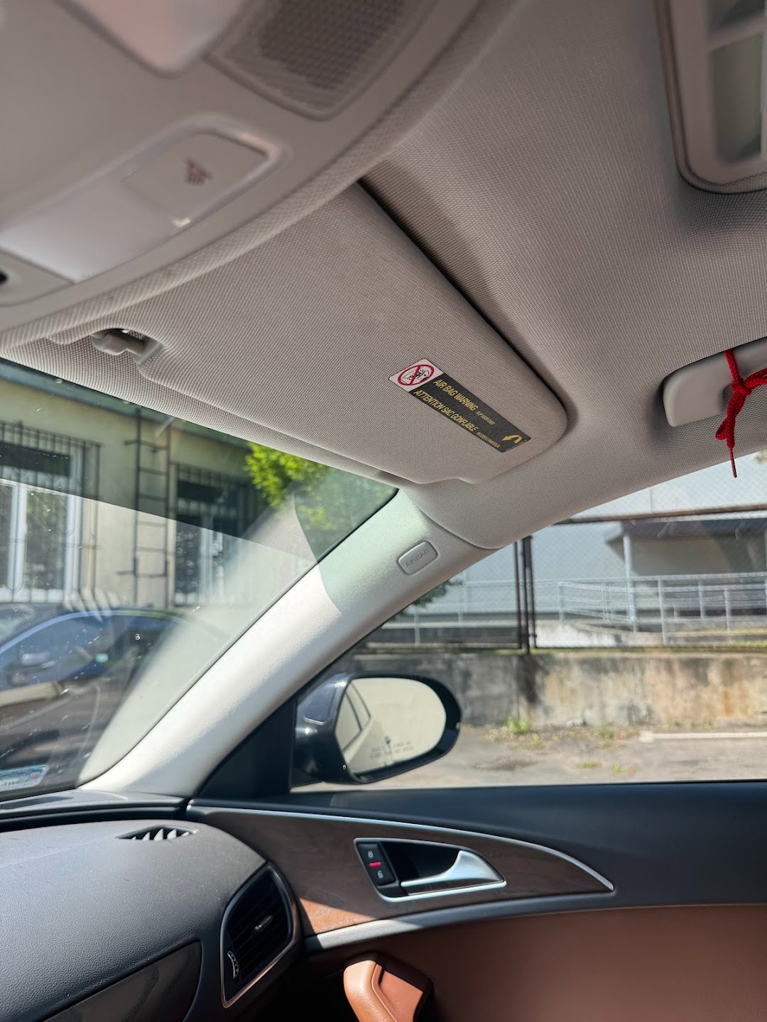 Wnętrze samochodu Audi z widoczną podsufitką, osłoną przeciwsłoneczną z naklejką ostrzegawczą, lusterkiem bocznym i brązową tapicerką drzwi z drewnianym wykończeniem.