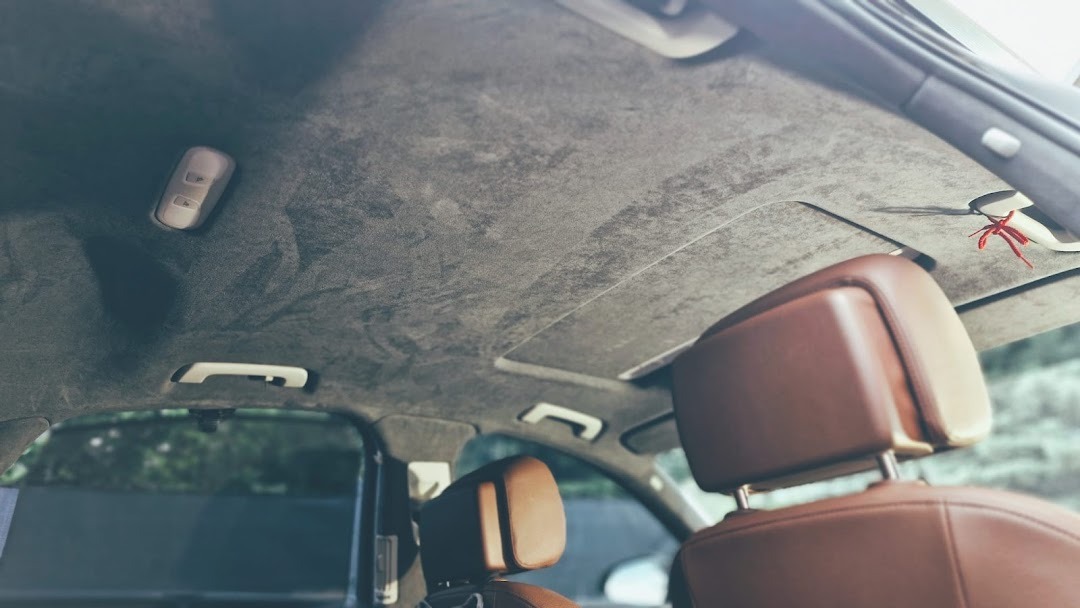 Wnętrze samochodu z nową, szarą podsufitką zamszową oraz brązowymi skórzanymi zagłówkami, widok z dołu.