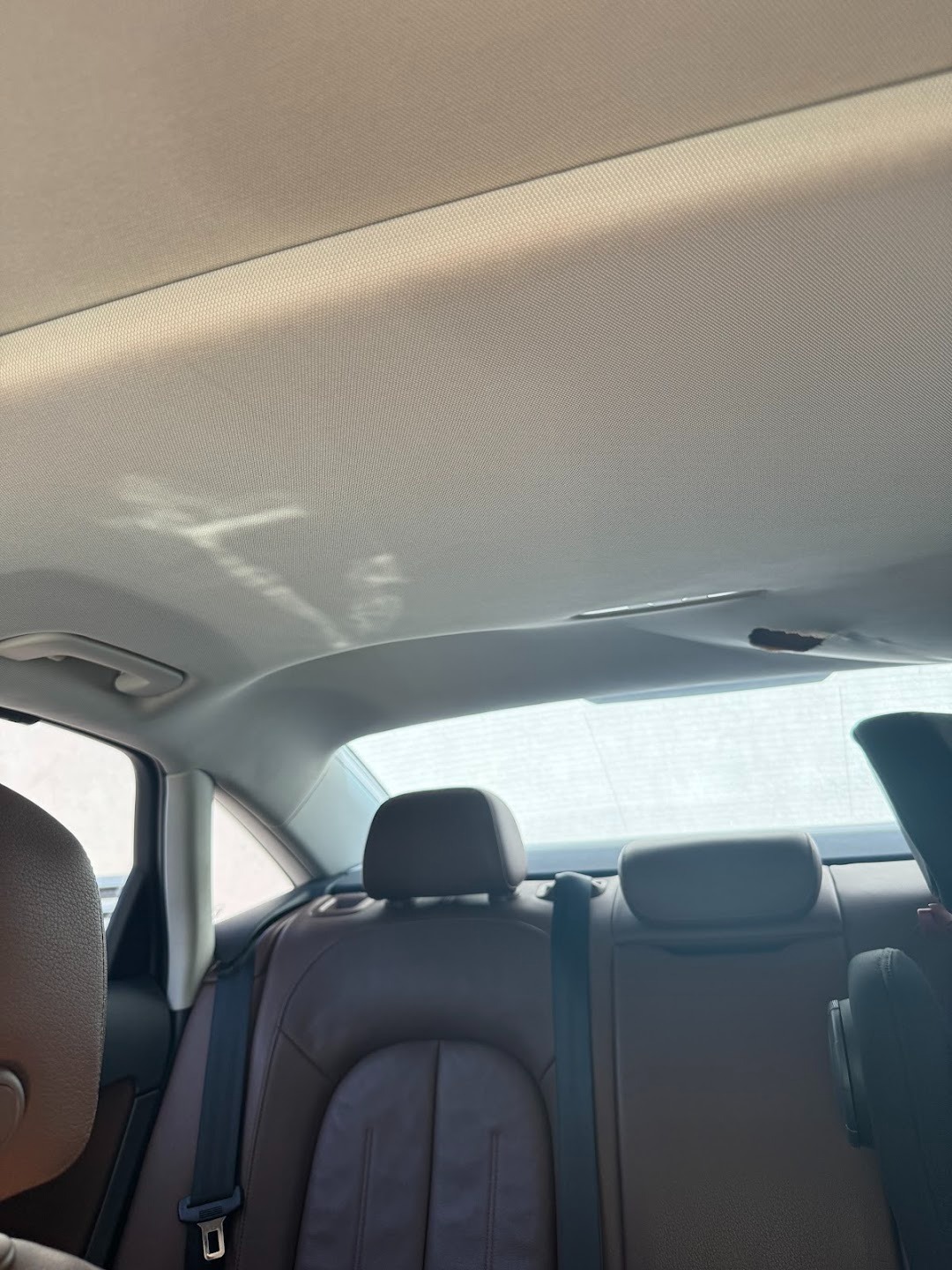 Wnętrze samochodu z brązową skórzaną tapicerką tylnych siedzeń i jasną podsufitką, widok z perspektywy pasażera.