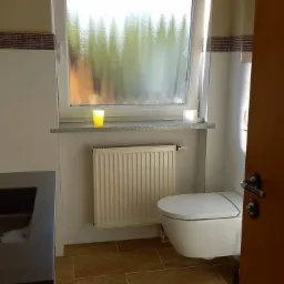 Nowoczesna łazienka z podwieszaną toaletą, grzejnikiem panelowym pod oknem z granitowym parapetem i dekoracyjną mozaiką pod sufitem.