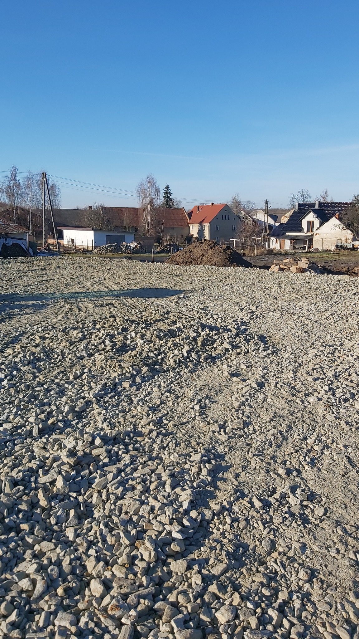 Teren budowy wyrównany gruzem pod budowę domu jednorodzinnego w słoneczny dzień, widoczne ślady opon i niewielki kopiec ziemi.