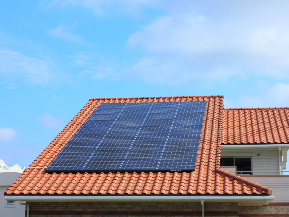 Panel fotowoltaiczny Kyocera na dachu z czerwonej dachówki, błękitne niebo w tle. Widok z dołu, podkreślający integrację z architekturą domu.