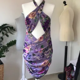 Fioletowa sukienka mini z kwiatowym wzorem na manekinie krawieckim z wycięciem na brzuchu, w tle drugi manekin i roślina doniczkowa.