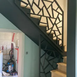 Nowoczesne schody z drewnianymi stopniami i geometryczną, metalową balustradą w kolorze czarnym, widok z dołu.