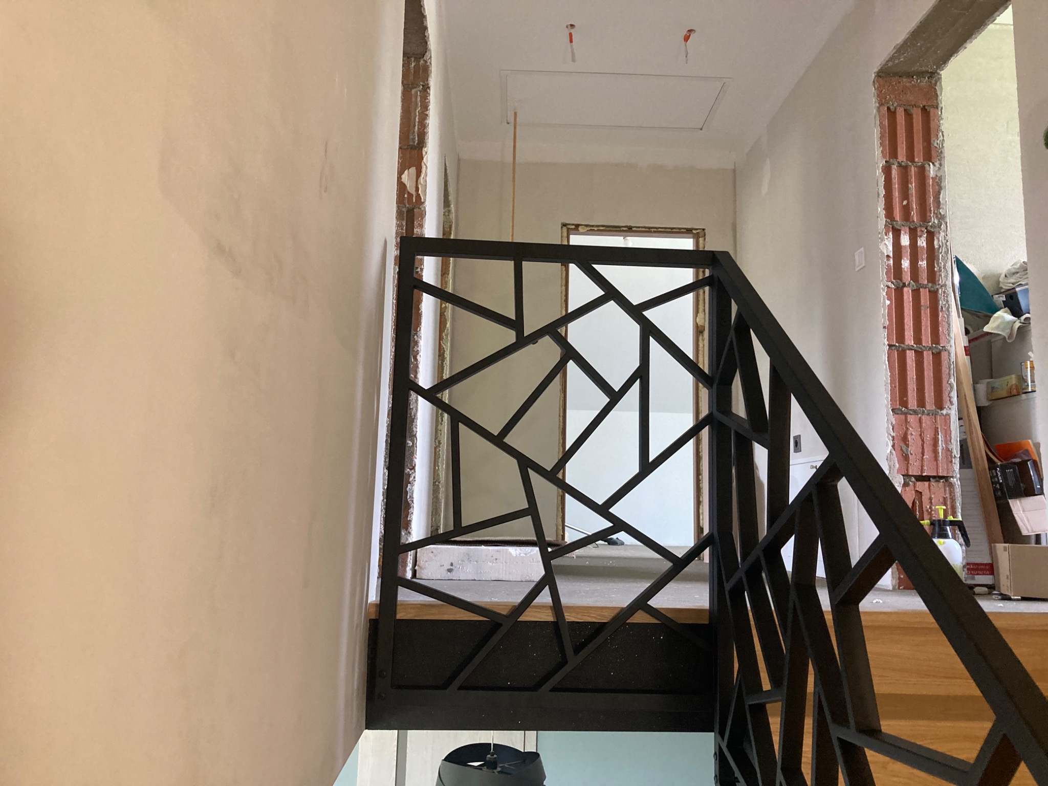 Nowoczesna, geometryczna balustrada schodowa z czarnego metalu w surowym wnętrzu, widoczne niedokończone ściany i fragmenty cegieł.