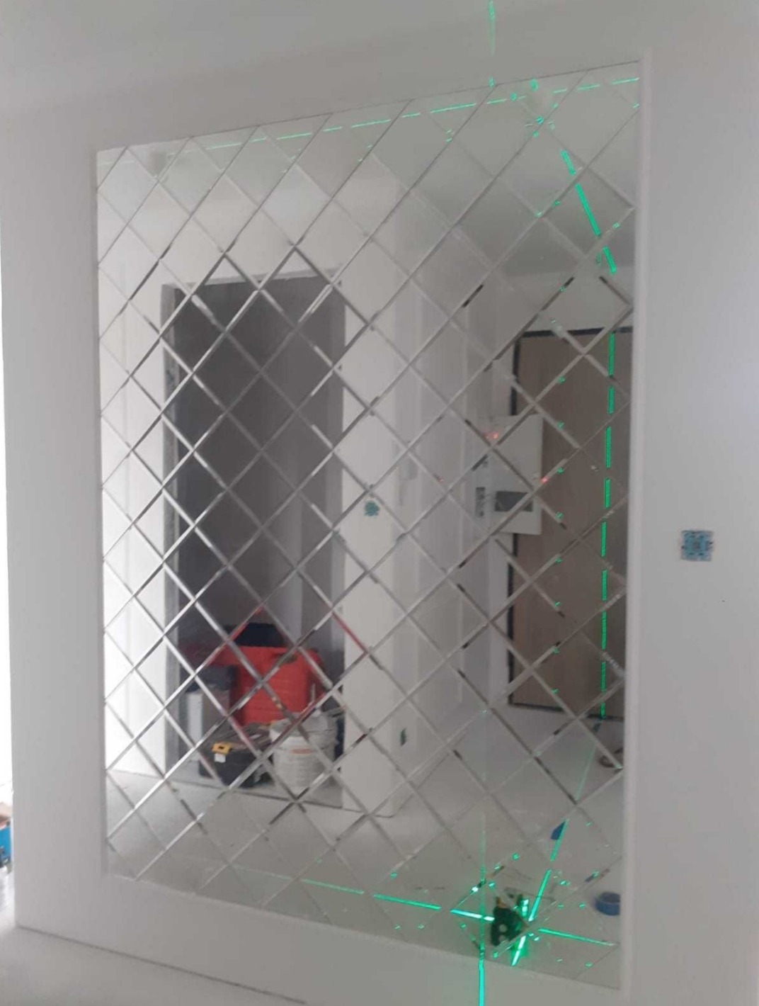 Montaż dekoracyjnego lustra z romboidalnych elementów w Kwidzynie, widoczny laser krzyżowy wyznaczający linie, odbicie pokoju w lustrze.