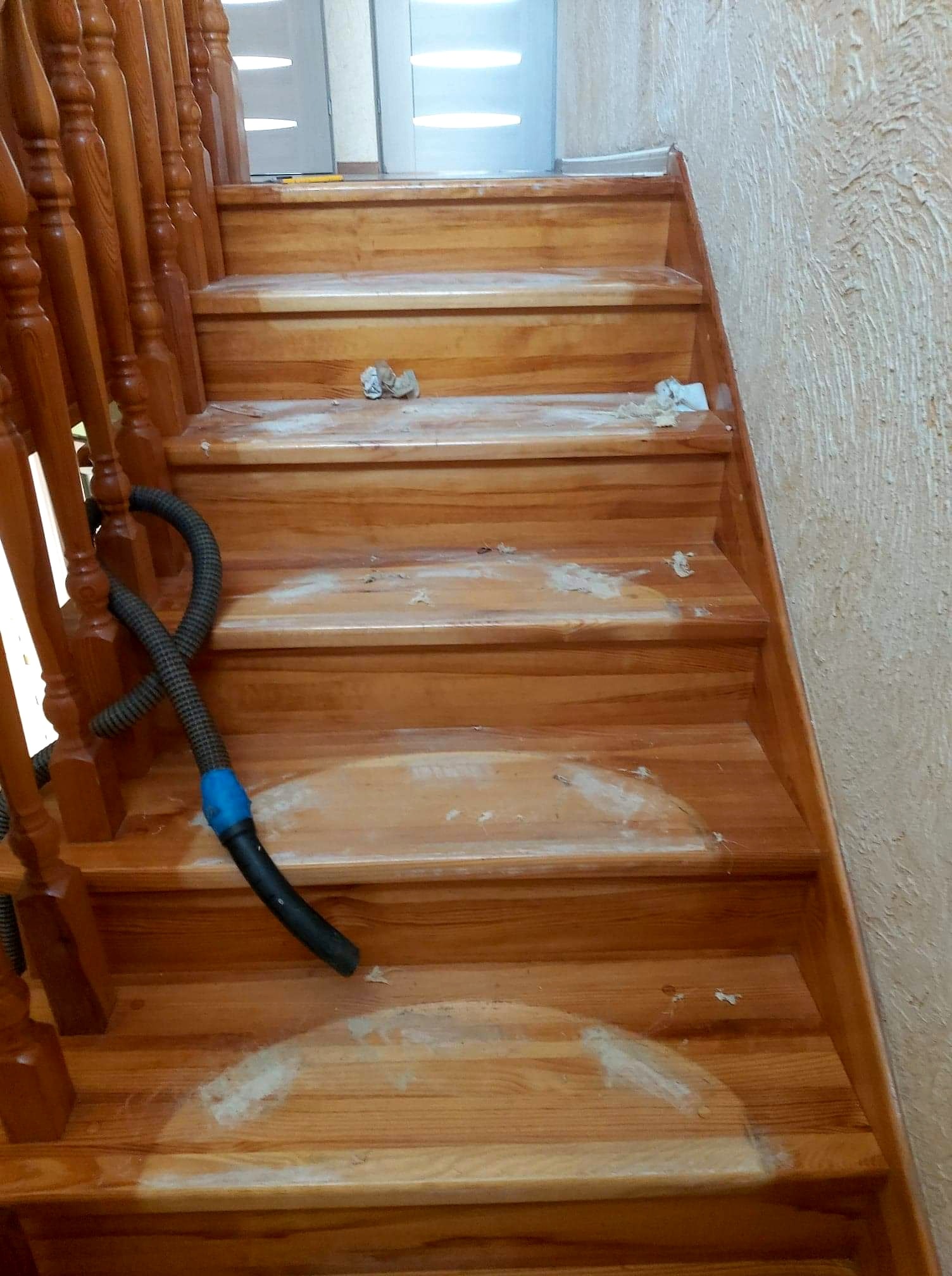 Drewniane schody w trakcie renowacji w Myślenicach, widoczne ślady po szlifowaniu i wąż odkurzacza do zbierania pyłu.