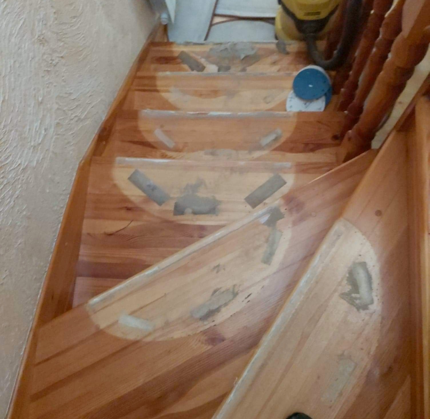 Cyklinowanie drewnianych schodów w trakcie renowacji, widoczne ślady po taśmie malarskiej, szlifierka i odkurzacz w tle.