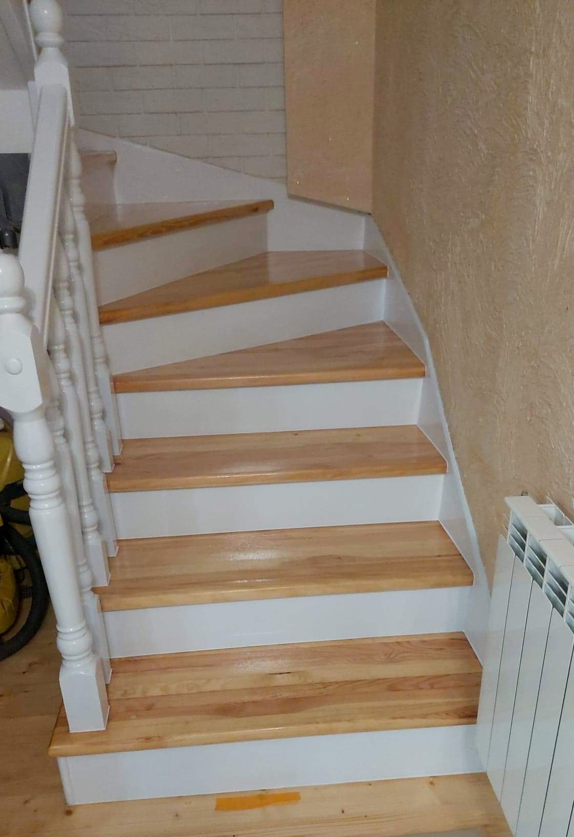 Drewniane schody z białymi podstopnicami i balustradą, widok z dołu, obok grzejnik.