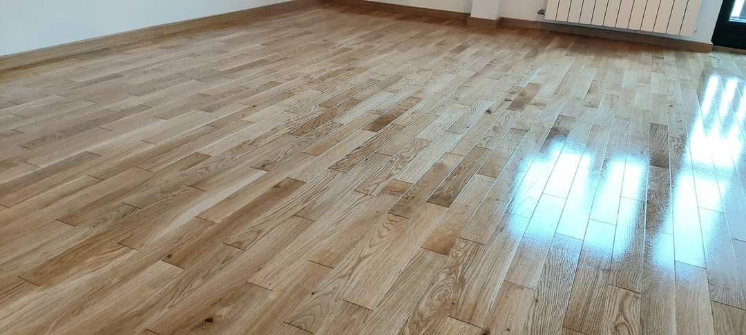 Świeżo położony, lakierowany parkiet z naturalnego drewna dębowego ułożony w jodełkę, widoczny fragment ściany i grzejnika.