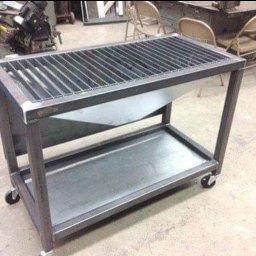 SpawLeks producent meble w stylu Loft usługi spawalnicze metoda TIG spawania aluminium oraz stali - Metalowa konstrukcja na kółkach z rusztem na górze i półką na dole, spawana z profili stalowych, w tle warsztat.