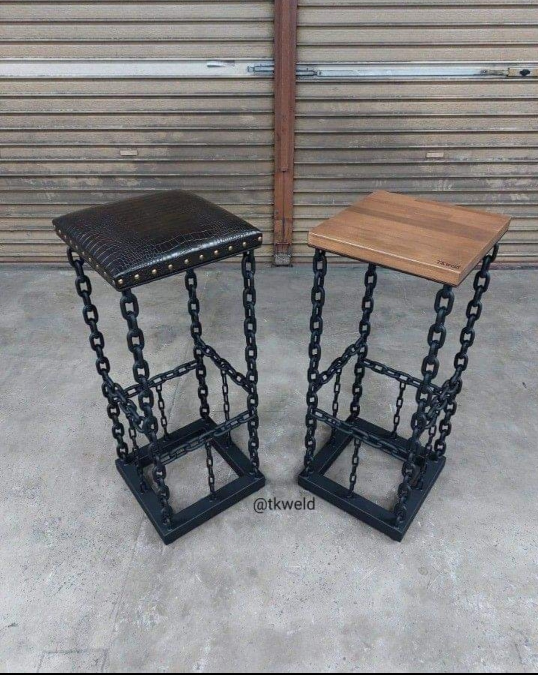 Dwa unikalne stołki barowe z czarnych łańcuchów i podstaw spawanych, jeden z siedziskiem z imitacji skóry krokodyla z ćwiekami, drugi z drewnianym siedziskiem, na tle metalowej rolety.