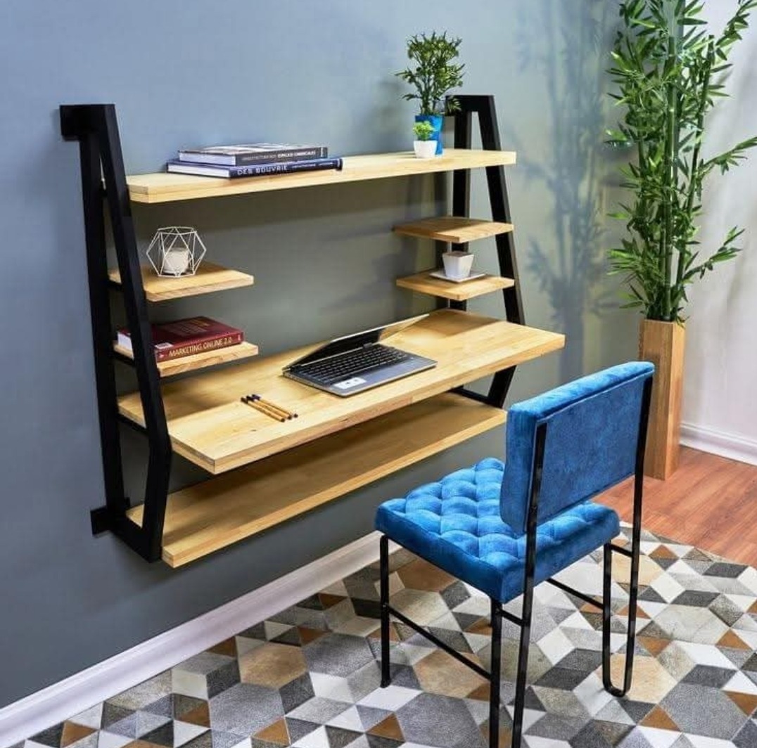 Nowoczesne biurko wiszące z półkami na metalowej ramie, laptop, niebieskie krzesło na tle wzorzystego dywanu.