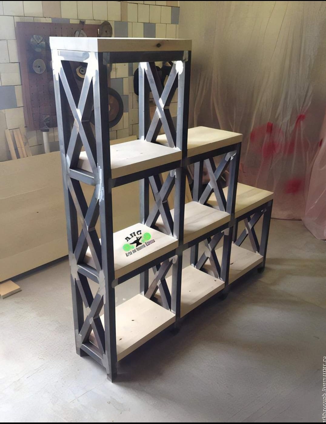 Metalowa konstrukcja regału z drewnianymi półkami w stylu industrialnym, z widocznymi spawami i logo na jednej z półek, na tle warsztatu.