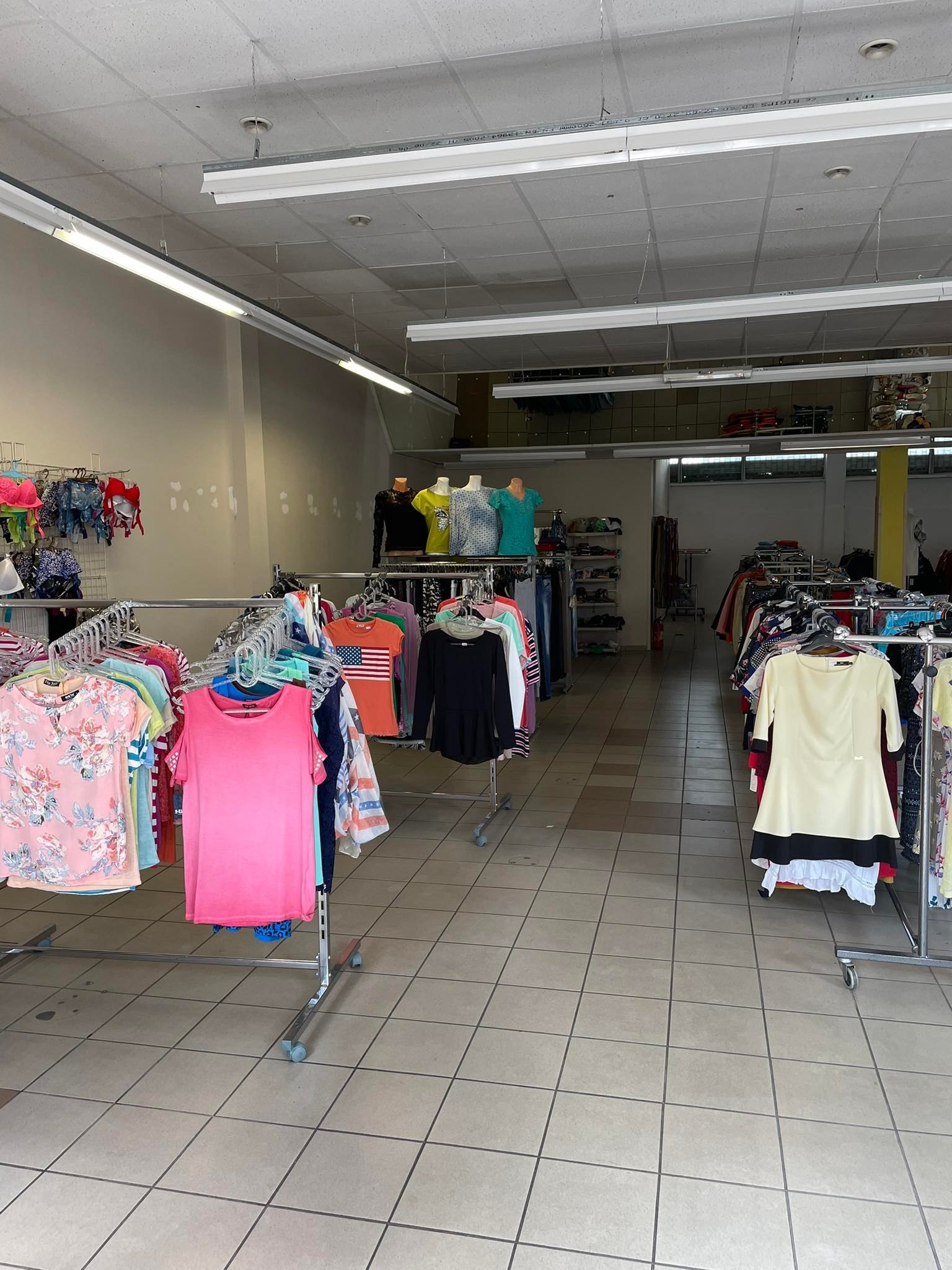 Wnętrze sklepu odzieżowego z ubraniami na wieszakach, widoczne manekiny i oświetlenie sufitowe.