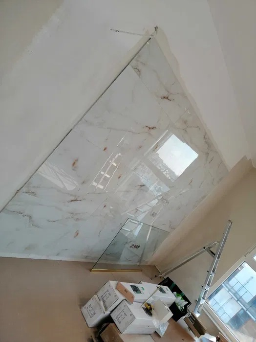 Montaż marmurowej okładziny ściennej z widocznymi elementami mocującymi, niezabezpieczonym szkłem i kartonami na podłodze, drabina oparta o ścianę.