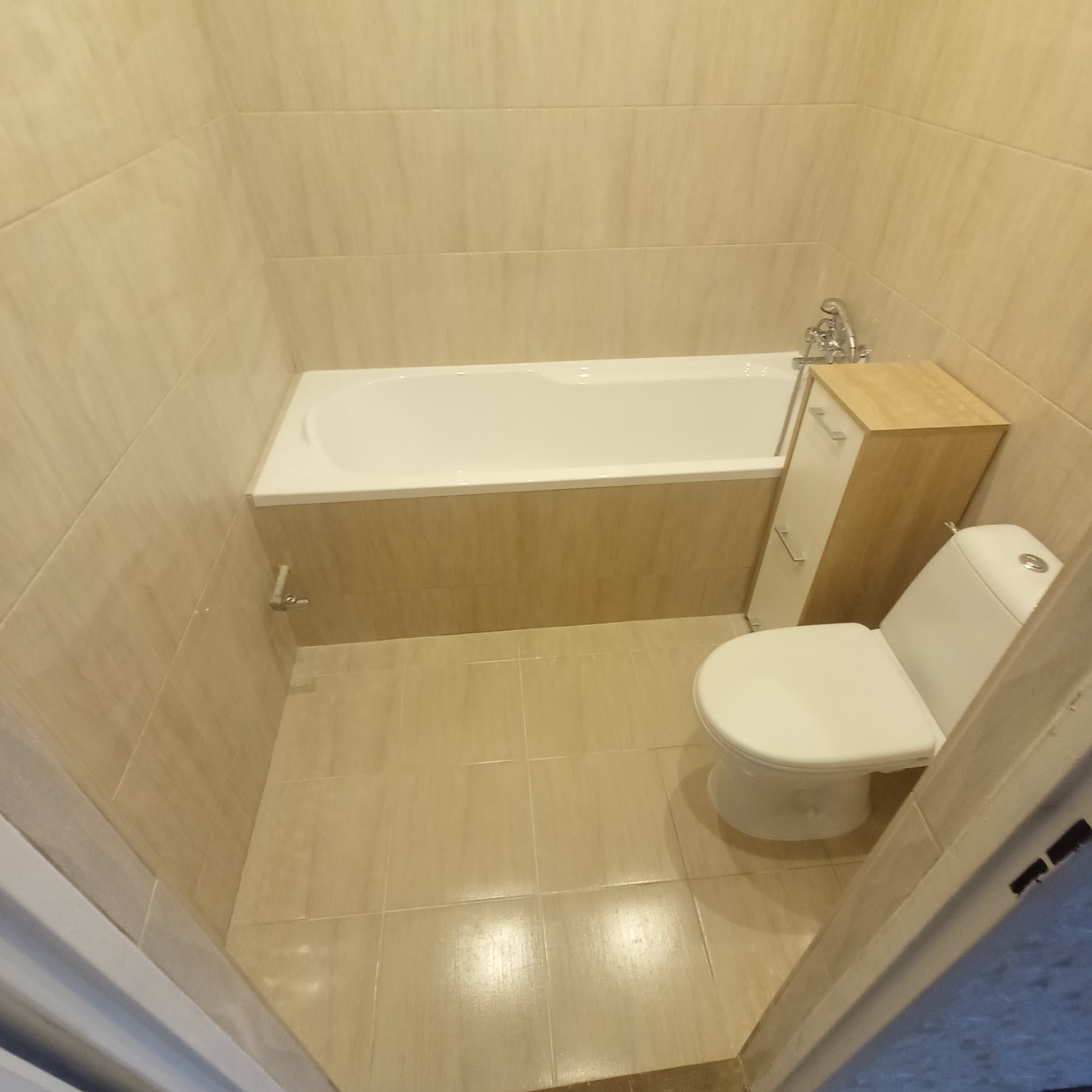 Wykończona łazienka w beżowych płytkach z białą wanną, toaletą i szafką pod umywalką, widok z góry na całe pomieszczenie.