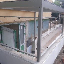 Anatsteel Sp. z o. o. - Zadaszone wejście do budynku w Szczecinie z rampą dla niepełnosprawnych, zabezpieczoną szklanymi balustradami i metalową konstrukcją.